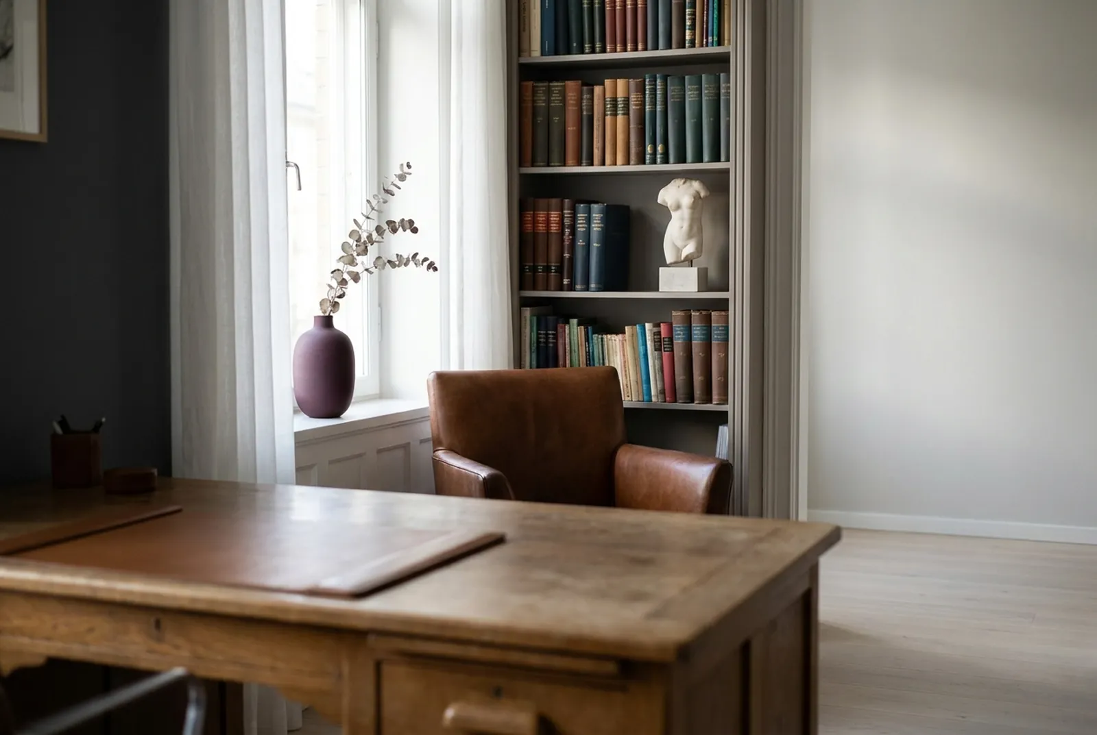 Consultório silencioso com mesa de madeira, poltrona de couro, estante de livros e janela com cortina clara